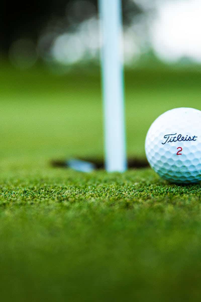 A close-up shot of a Titleist golf ball close to the hole on a green golf course.